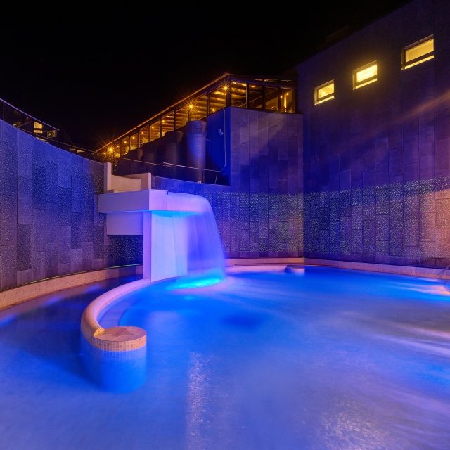 Nördliches Außenbecken im Thermalbad inklusive Wasserfall bei Nacht mit stimmiger Beleuchtung